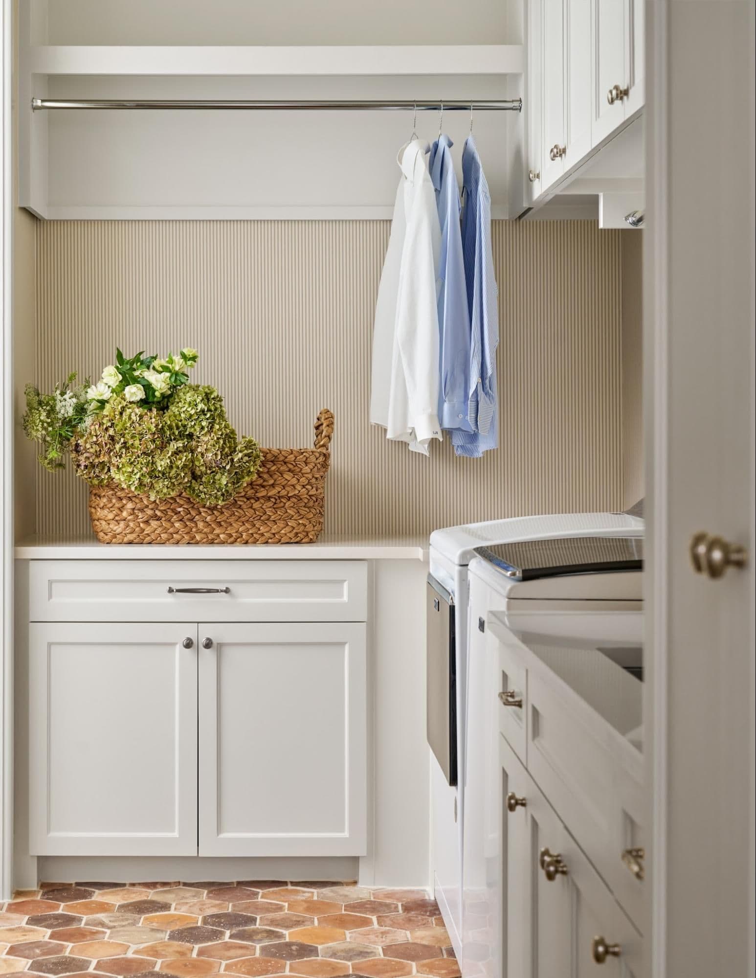 Laundry closet with hanging rod, folded linens, and a woven basket of flowers