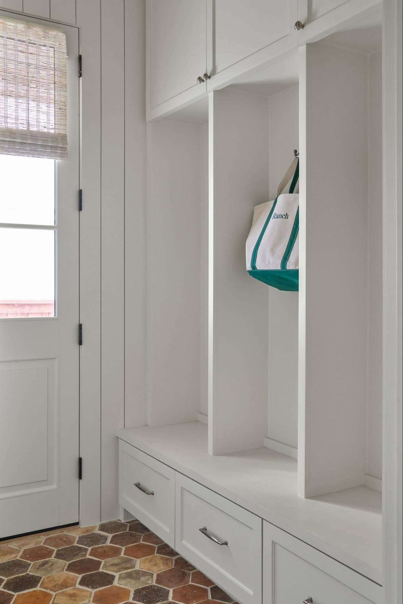 White mudroom lockers with hooks and a woven tote bag hanging inside